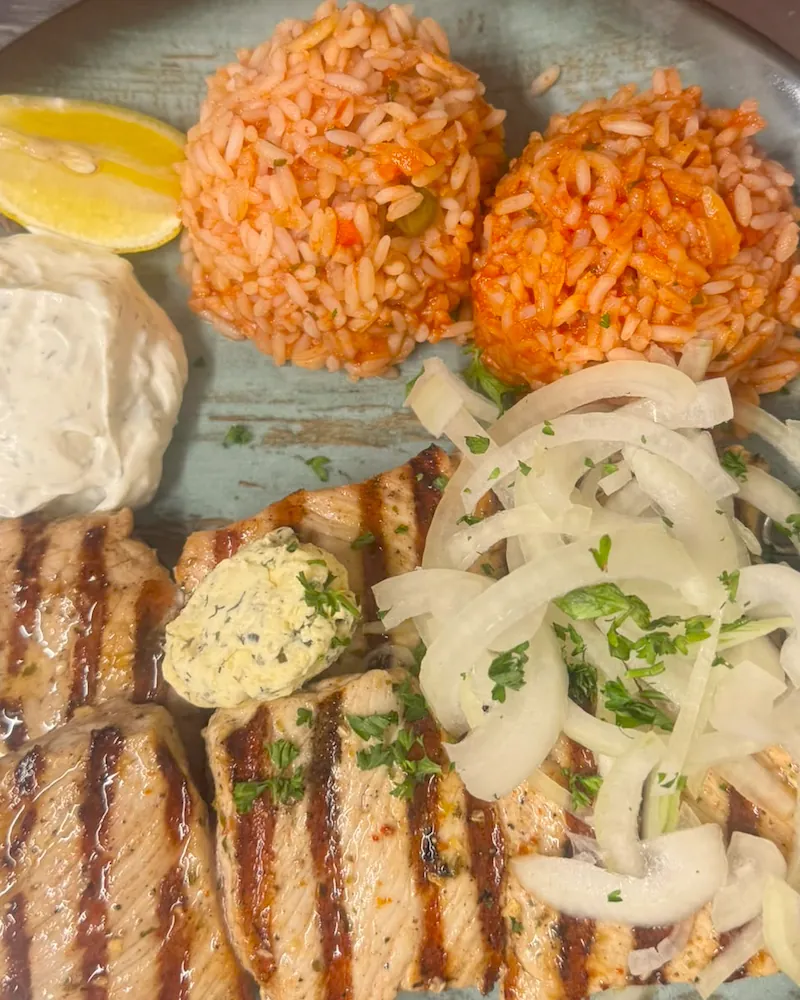 Zwei Suflaki-Spieße vom Grill mit Kräuterbutter, Zwiebeln, Tomatenreis und Tsatsiki